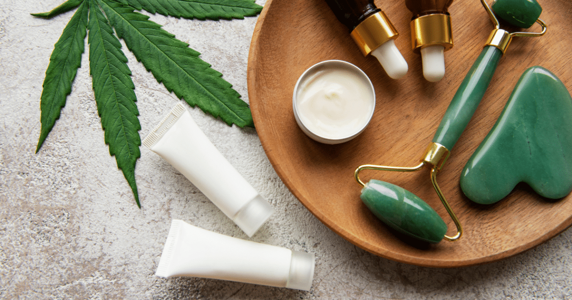 Bottles of CBD oil, a marijuana leaf and a derma roller on a wooden platter.