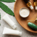 Bottles of CBD oil, a marijuana leaf and a derma roller on a wooden platter.